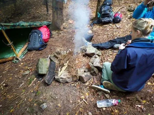 Kleine Flamme mit Rauch in einem Steinkreis, Person sitzt daneben