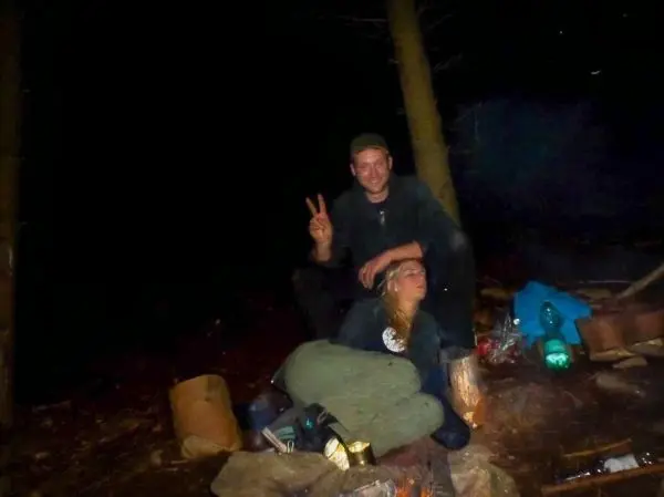 Kleines Bodenfeuer brennt im Wald, zwei Personen sitzen daneben