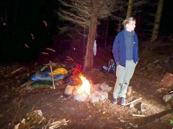 Kleines Bodenfeuer brennt zwischen Bäumen, Person steht daneben