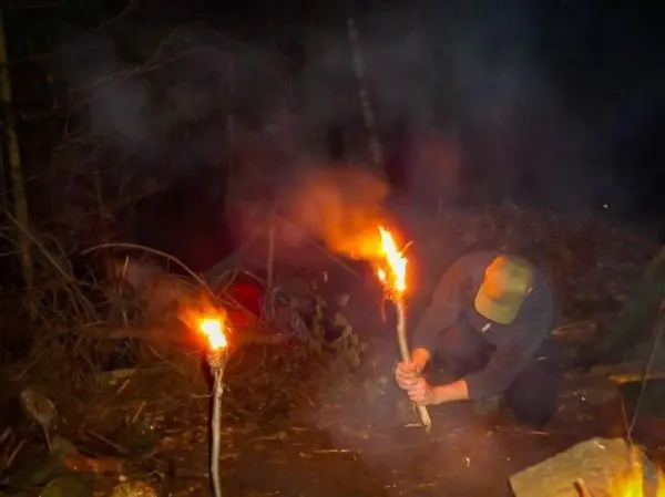 Mann hält brennenden Stock und bereitet Feuerstelle vor
