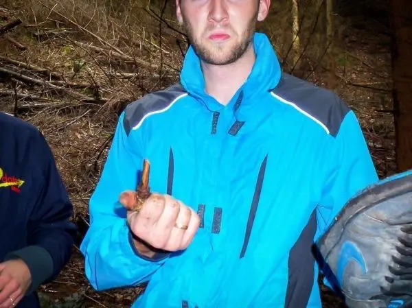 Mann hält einen kleinen Holzstock in der Hand, umgeben von Wald