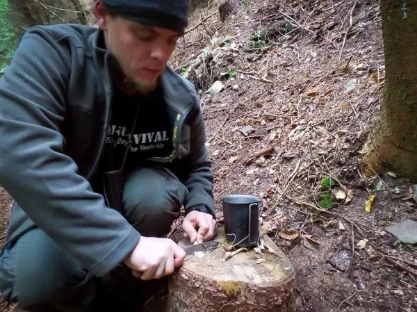 Messer schneidet Zunder auf einem Baumstumpf neben einem Kocher