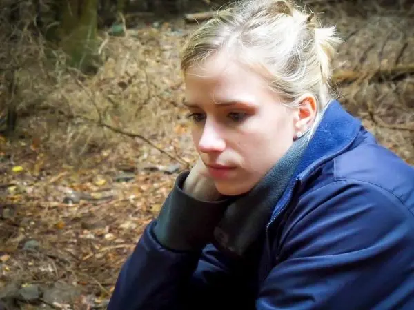 Nachdenkliche Person sitzt im Wald auf dem Boden zwischen Laub und Ästen