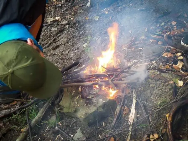 Person beugt sich über ein brennendes Feuer aus Ästen