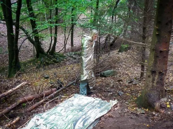 Person in Rettungsdecke steht neben einer reflektierenden Unterlage im Wald