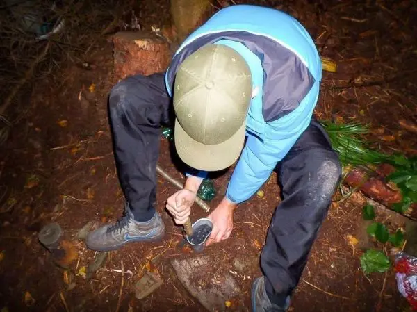 Person mischt Materialien in einem Behälter auf dem Waldboden