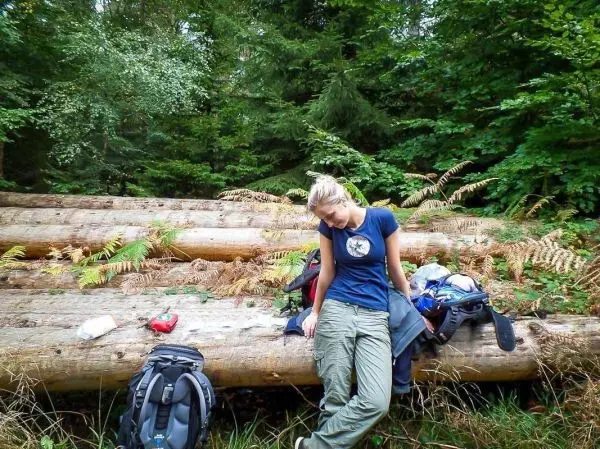 Person sitzt auf Baumstamm und schaut nach unten beim Wandern