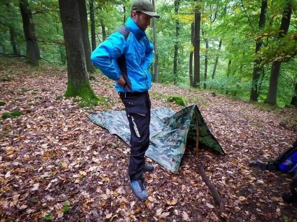 Person steht neben einer camouflagefarbenen Plane im Wald
