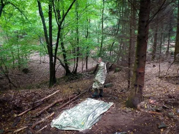 Person trägt eine Rettungsdecke und steht neben einer reflektierenden Unterlage im Wald