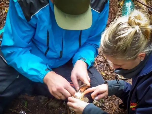Person zündet Feuer mit Zunder im Wald beim Survival Training