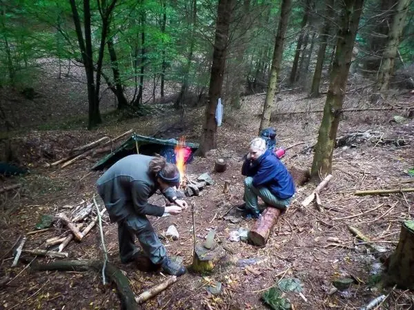 Person zündet Feuerstelle an, während andere Person sitzt
