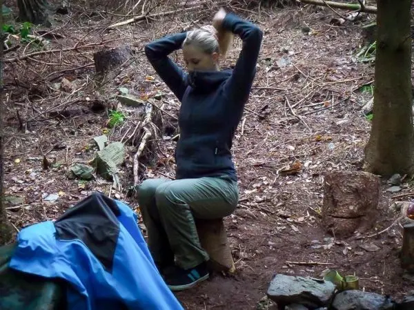 Sitzende Person auf einem Baumstumpf bindet ihre Haare zusammen