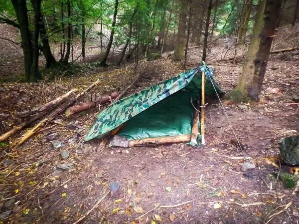Tarp-Notunterkunft aus einer Plane und Ästen im Wald aufgebaut
