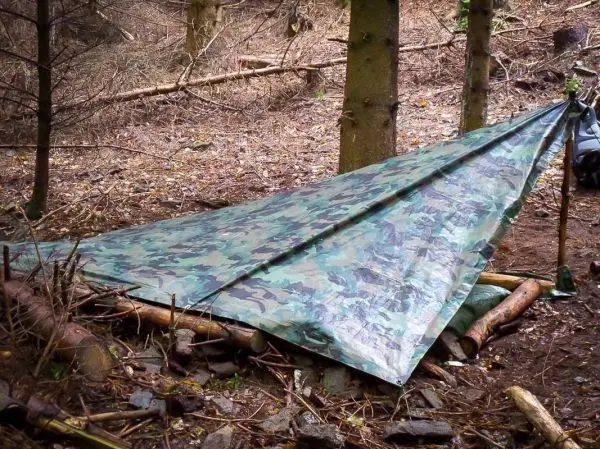 Tarp-Notunterkunft ist zwischen zwei Bäumen mit Holzstützen aufgebaut