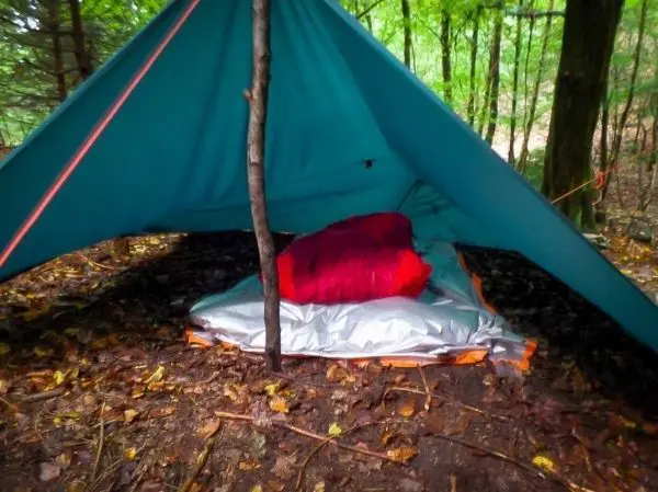 Tarp-Notunterkunft mit Schlafsack auf isolierender Unterlage im Wald