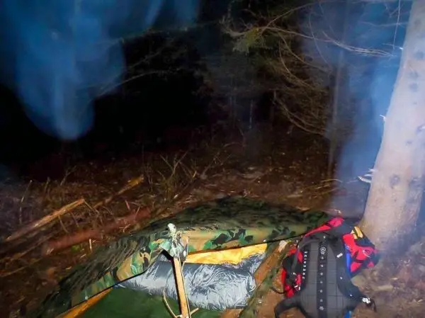 Tarp-Notunterkunft mit Schlafsack und Rucksack unter Bäumen im Wald