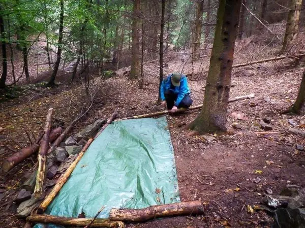 Tarp-Notunterkunft wird mit Ästen und Steinen stabilisiert