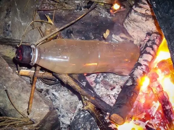 Wasserflasche erhitzt über einem kleinen Feuer aus Holzscheiten