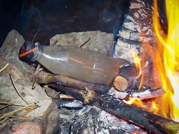 Wasserflasche erhitzt über einem offenen Feuer zwischen Steinen und Holz