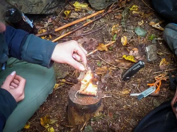 Zunder glimmt auf einem Holzstück, während eine Hand Funken erzeugt
