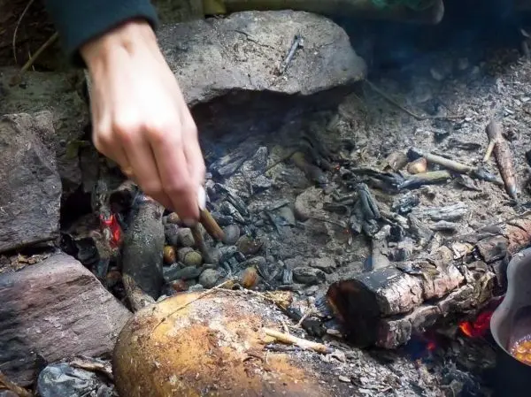 Zunder glimmt in der Feuerstelle, Hand bewegt sich zur Glut