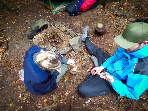 Zunder glimmt in einem kleinen Feuerkreis, während eine Person mit einem Feuerstahl Funken erzeugt
