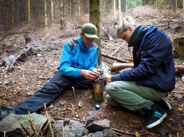 Zunder wird mit einem Feuerstahl entzündet, während zwei Personen auf dem Boden sitzen