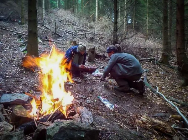 Zwei Personen bereiten etwas am Boden vor, während ein Feuer brennt