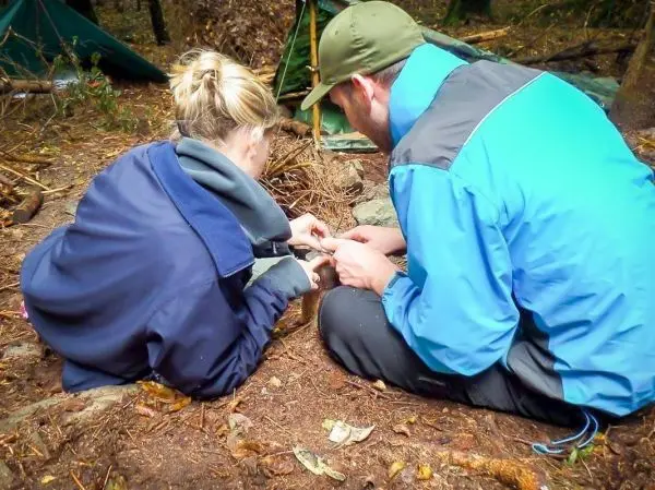 Zwei Personen bereiten Zunder auf dem Boden vor, um ein Feuer zu entzünden