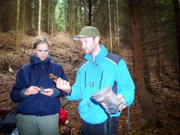 Zwei Personen betrachten Ausrüstung im Wald, eine hält ein Gerät, der andere einen Schuh