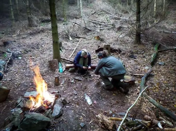 Zwei Personen knien am Boden und bereiten Zunder neben einem kleinen Feuer