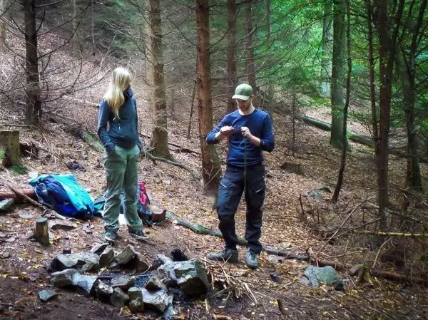 Zwei Personen stehen im Wald neben einem Steinkreis, einer hält ein Messer