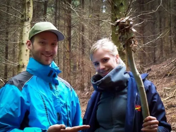 Zwei Personen zeigen auf einen Stock mit einem Zundernest in einem Wald