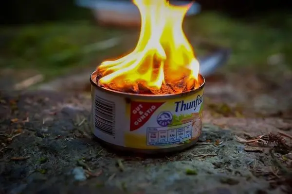 Brennende Dose mit Inhalt auf einem Untergrund aus Erde und Gras