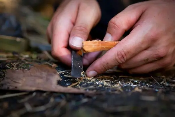 Holzstück wird mit einem Messer bearbeitet, um Zunder zu erzeugen