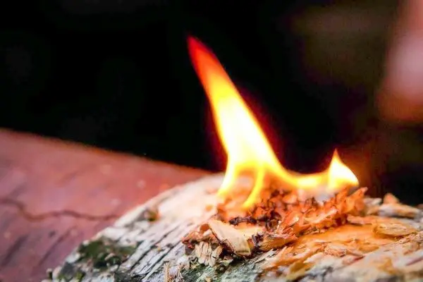 Kleine Flamme brennt auf Zunderstück aus Holz