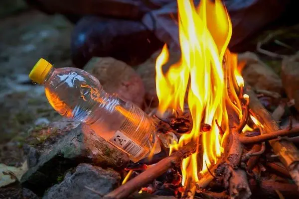 Kleine Flamme brennt zwischen Steinen mit Wasserflasche in der Nähe