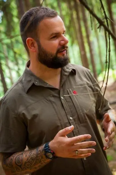 Mann gestikuliert im Wald, umgeben von Bäumen und Ästen