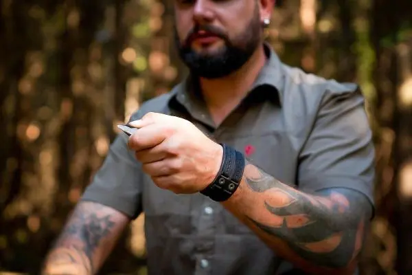 Mann hält ein Messer in der Hand, umgeben von Bäumen im Wald