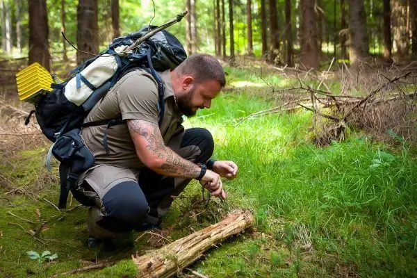 Mann kniet im Wald und bearbeitet einen Holzstock mit einem Messer