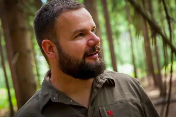 Mann mit Bart steht im Wald zwischen Bäumen