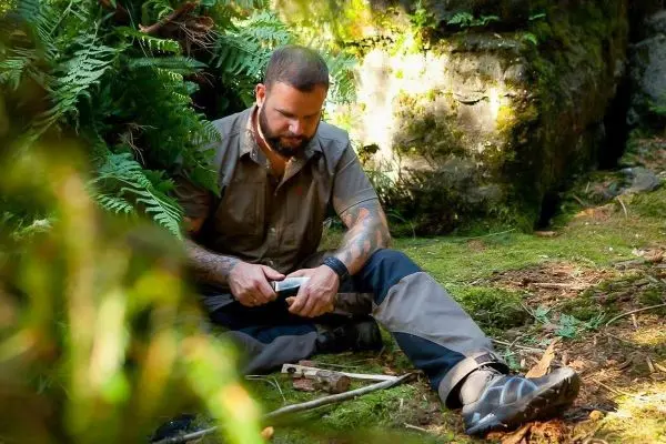 Mann schnitzt mit einem Messer Holzstücke im Wald