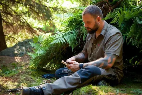 Mann sitzt im Wald und schnitzt mit einem Messer an einem Holzstück