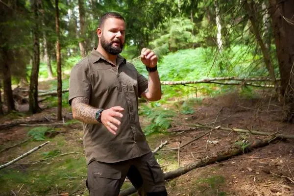 Mann steht im Wald und gestikuliert mit den Händen