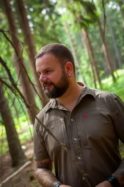 Mann steht im Wald zwischen Bäumen und schaut nachdenklich zur Seite