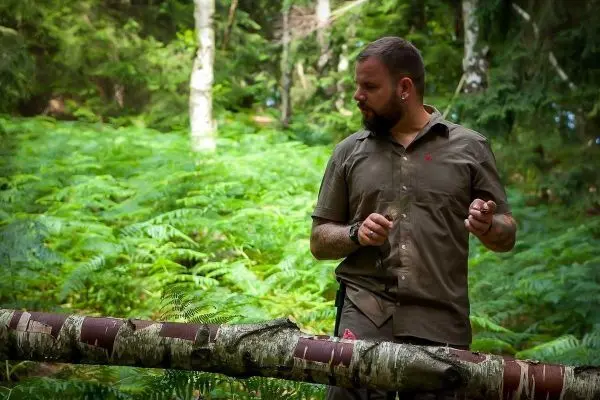 Mann steht neben einem umgestürzten Baumstamm im Wald und hält ein Messer