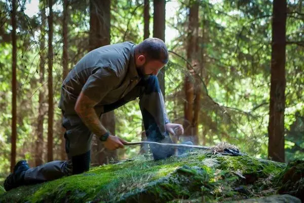 Mann zündet Zunder mit einem Feuerstahl auf moosbedecktem Stein an