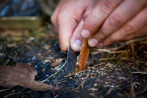 Messer schabt Rinde von einem Holzstück auf dem Boden