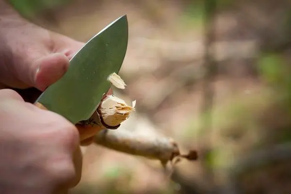 Messer schneidet Holzstück und entfernt Späne im Wald