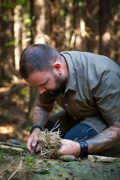 Person bereitet Zunder aus Gras im Wald vor beim Survival Training